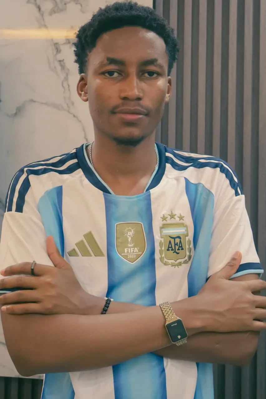 A young man in the Argentina world champions jersey, arms folded, gaze steady and unhurried